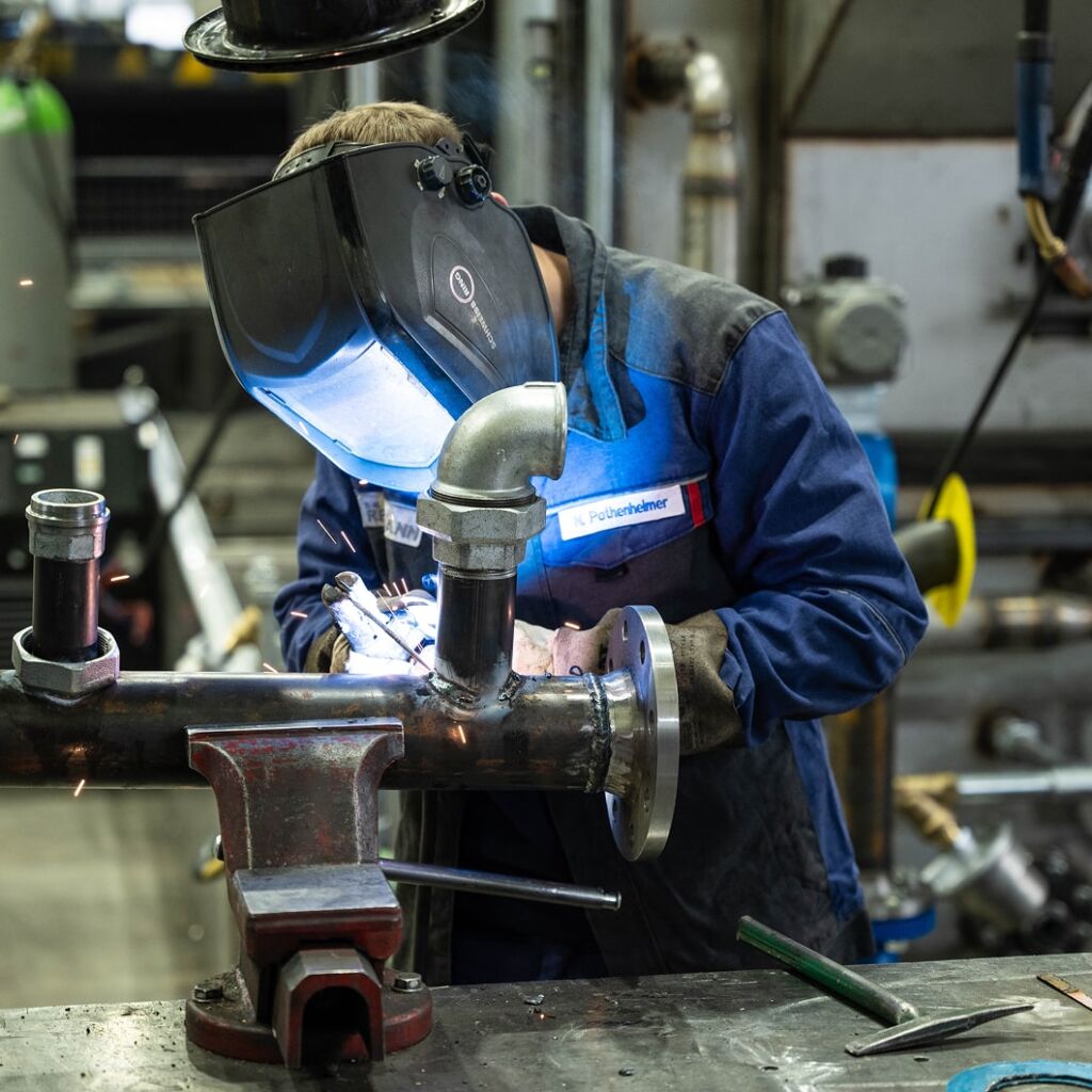 Ein Industriemechaniker bei Renzmann schweißt an der Verrohrung einer Teilewaschmaschine.