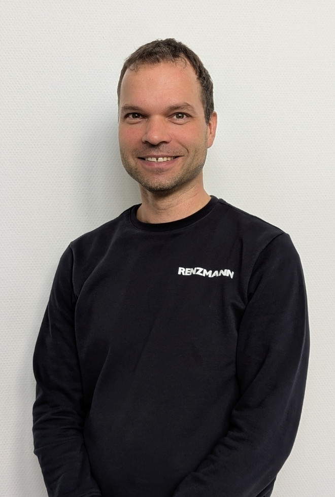 Mitarbeiter im RENZMANNN Pullover lächelt vor weißer Wand