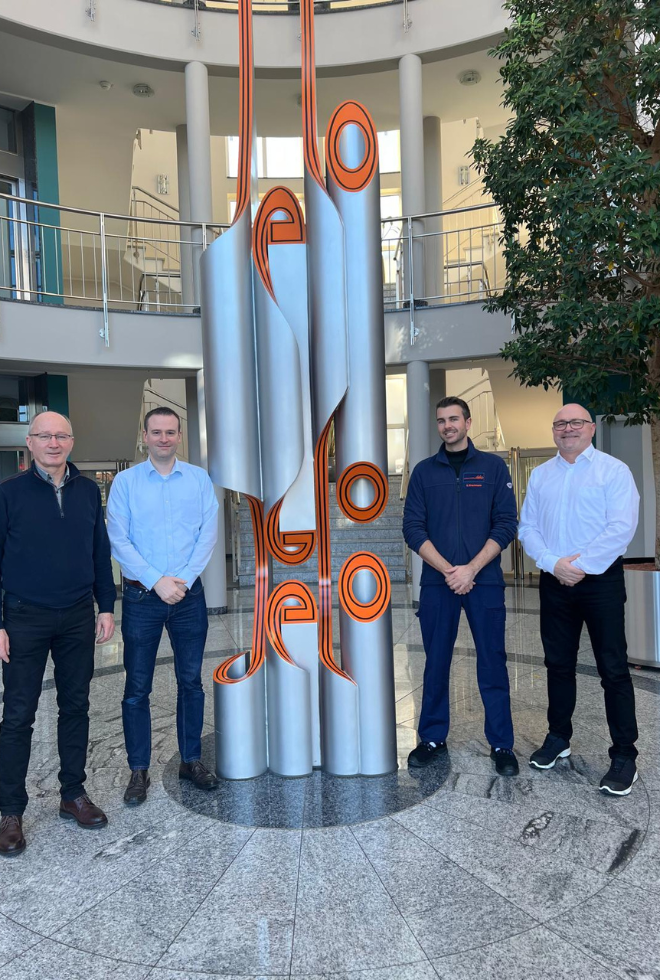 Vier Personen vor moderner Skulptur in Firmenfoyer