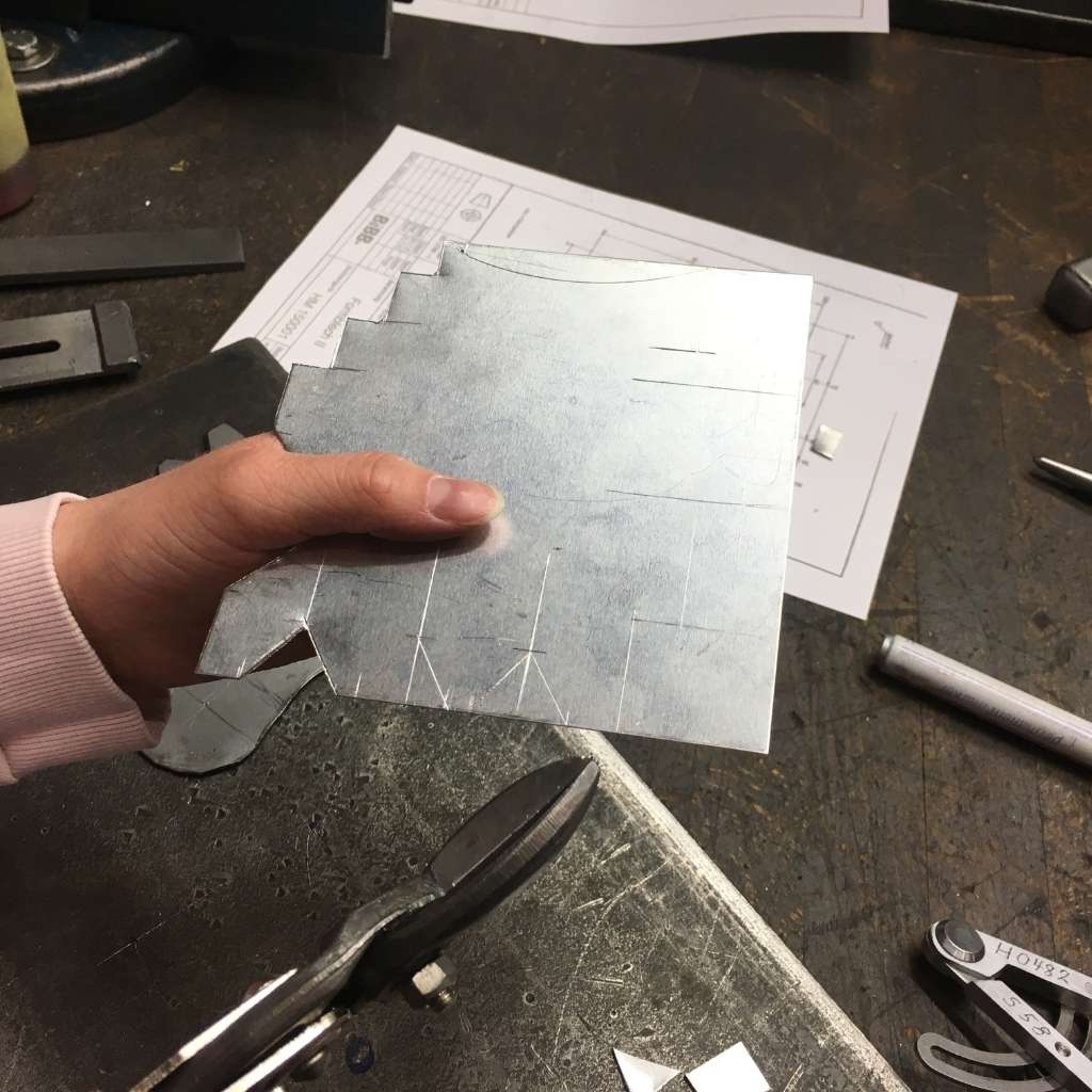 Hand hält zugeschnittenes Metallblech auf Werkbank