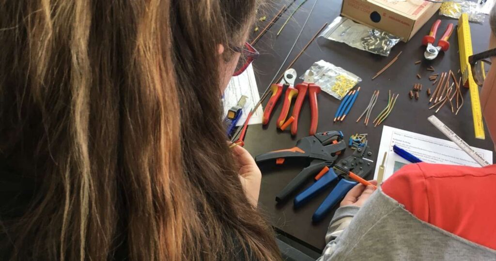 Schülerin arbeitet mit Werkzeug und Kabeln in der Lehrwerkstatt